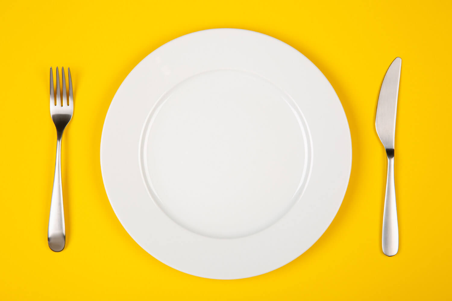 Aerial view of a white plate with silverware on a yellow table at a restaurant