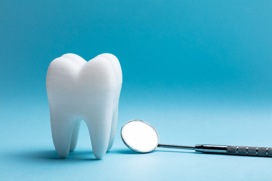 An extracted tooth next to a special dental mirror against a blue background