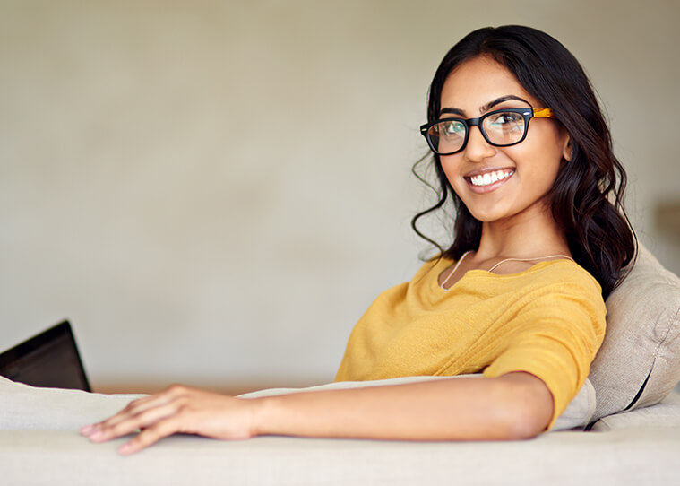 smiling woman sitting on the couch, looking at her computer