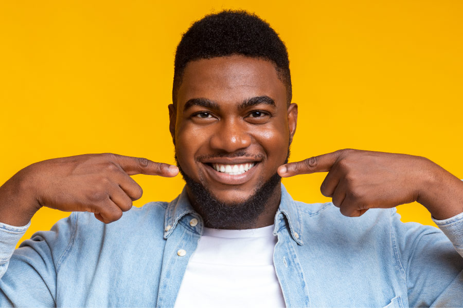 Dark-haired man smiles and points to his teeth after teeth whitening at Wedington Family Dental