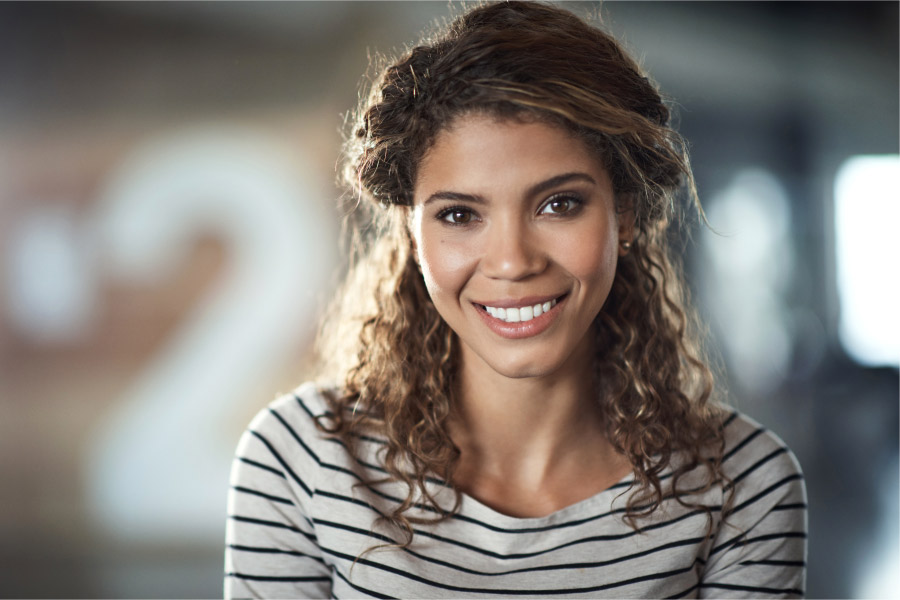 Curly-haired woman smiles at the dentist after receiving BOTOX to smooth wrinkles and fine lines and ease headaches