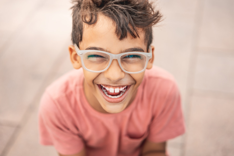 brunette boy in glasses smiles while wearing a salmon-colored t-shirt outside the dentist