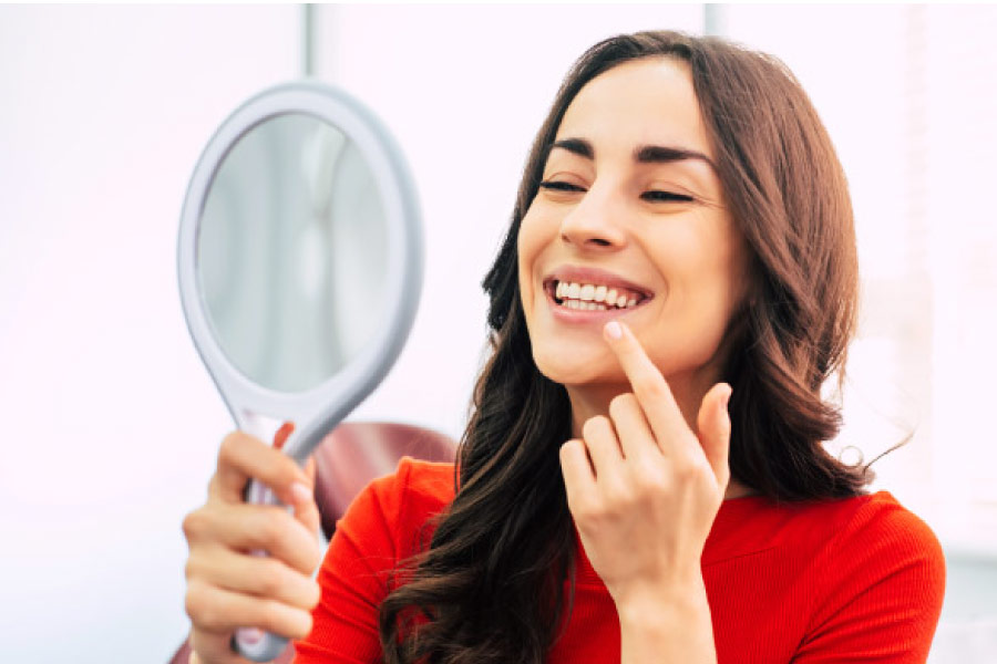 woman looks in a hand held mirror at her teeth whitening results