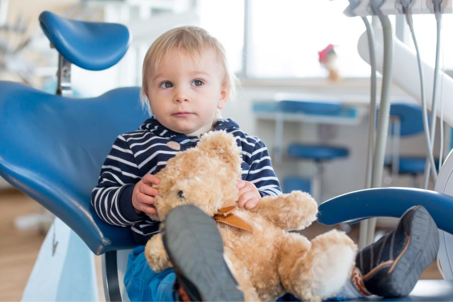 baby boy sitting in the dentist chair holding a stuffed bear